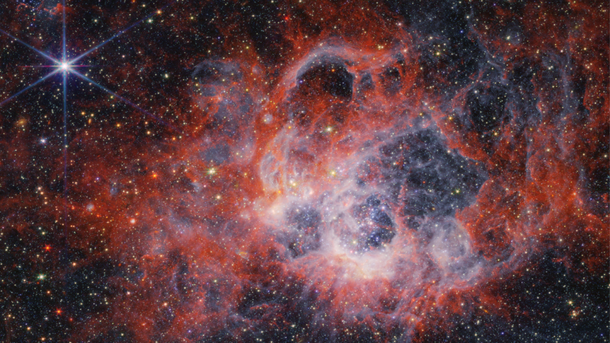  A James Webb Space Telescope image showing reddish hazy webs against a dark blue background. Toward the top left is a glare with the telescope's characteristic spikes. 