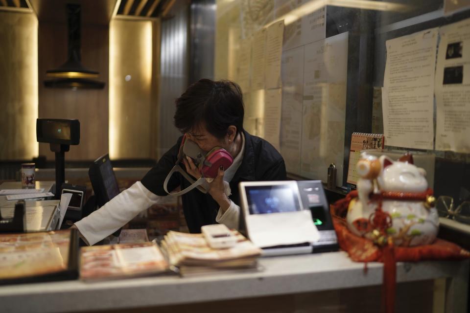 A cashier in a restaurant reacts to tear gas as police confront protesters on Christmas Eve in Hong Kong on Tuesday, Dec. 24, 2019. More than six months of protests have beset the city with frequent confrontations between protesters and police. (AP Photo/Kin Cheung)