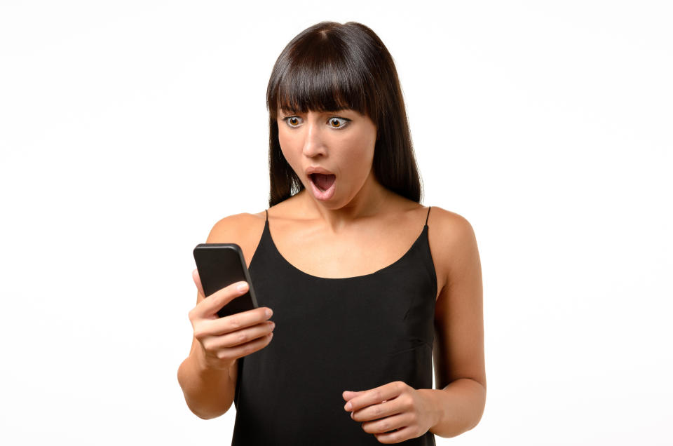 Horrified young woman looking at her mobile in shock as she reads a text message, isolated on white