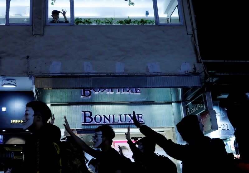 A woman in a shop waves to protesters wearing Guy Fawkes masks during an anti-government demonstration in Hong Kong