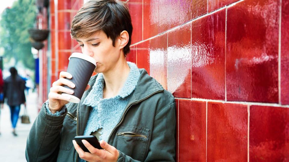 Stressed woman reading emails on her mobile phone with a frown while drinking coffee on her way to work.