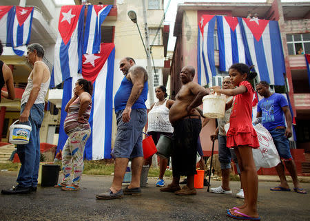 People line up for potable water from a government-run water tanker (not pictured) next to Cuban flags hung up to dry after Hurricane Irma caused flooding and a blackout, in Havana, Cuba September 11, 2017. REUTERS/Alexandre Meneghini