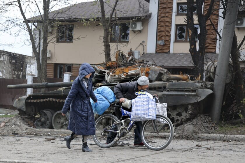 Local civilians walk past a tank destroyed during heavy fighting in an area controlled by Russian-backed separatist forces in Mariupol, Ukraine, Tuesday, April 19, 2022. Taking Mariupol would deprive Ukraine of a vital port and complete a land bridge between Russia and the Crimean Peninsula, seized from Ukraine from 2014. (AP Photo/Alexei Alexandrov)