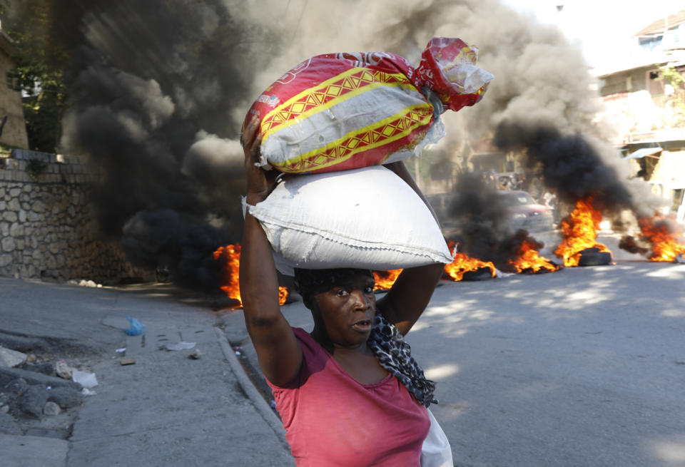 A woman walks past burning tires set on fire by protesters to call attention to the country's insecurity and demanding the resignation of the prime minister, in Port-au-Prince, Haiti, Thursday, Jan. 18, 2024. (AP Photo/Odelyn Joseph)