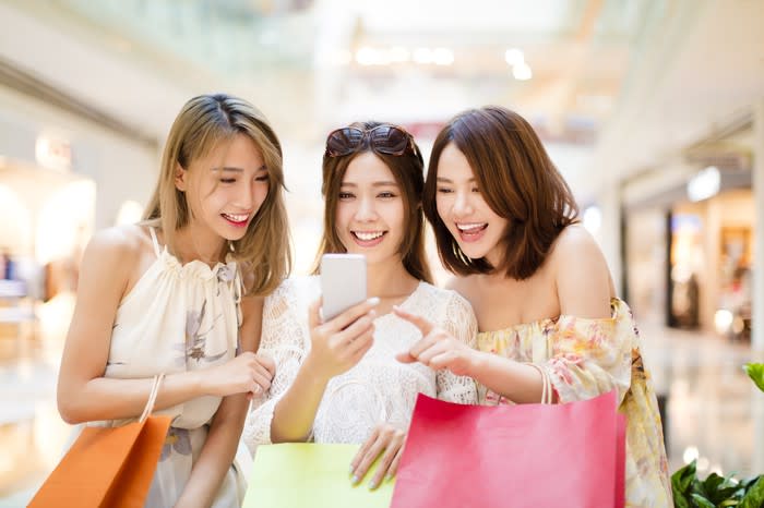 Three young women check their smartphone as they shop.