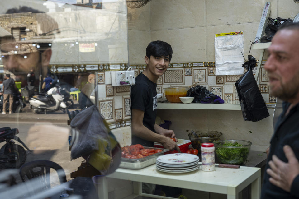 Mohammed Zuad Khaman, center, prepares kebabs at his family's cafe in one of Baghdad's poorer neighborhoods along King Ghazi Street on Monday, Feb. 27, 2023. Khaman is a talented footballer, but he says he cannot get an opportunity to play in any of Baghdad's amateur clubs because he does not have any "in" with the militia-related gangs that control sports teams in the city. (AP Photo/Jerome Delay)