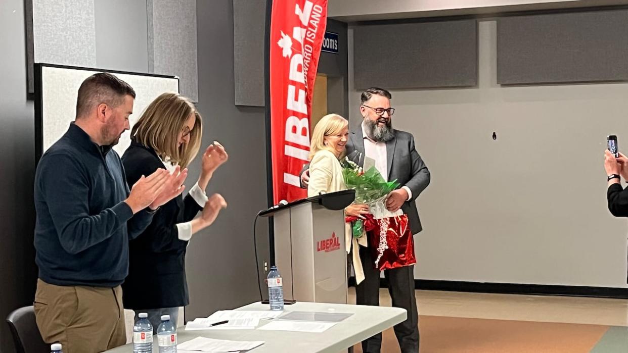 Hal Perry, the interim Liberal leader, presents a gift to former leader Sharon Cameron as party executives Zach Murphy and Katie Morello applaud during the annual general meeting Saturday. (Kerry Campbell/CBC - image credit)