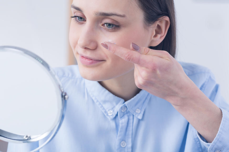 Woman inserting contact lens, sitting in front of a mirror