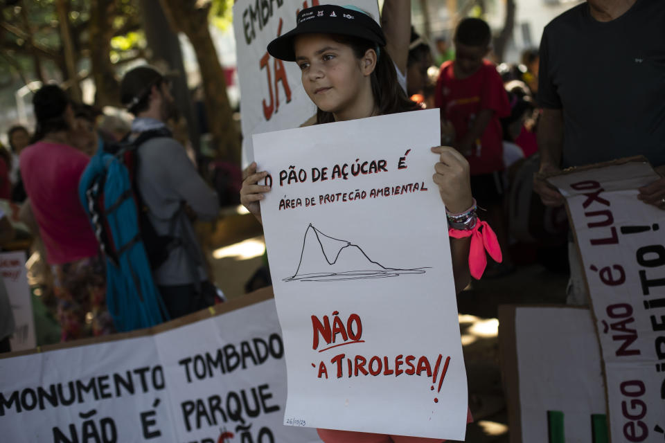 A child holds a sign that reads in Portuguese "Sugar Loaf Mountain is an environmental protection area. Not the zip line," during a protest against the installation of a zip line on Sugar Loaf Mountain, an iconic symbol of the city and UNESCO World Heritage Site, in Rio de Janeiro, Brazil, Sunday, March 26, 2023. (AP Photo/Bruna Prado)