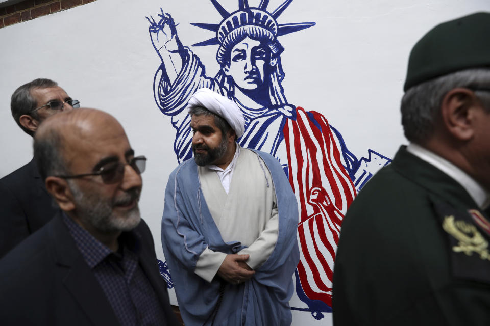A Shiite Muslim cleric stands in front of a satirical drawing of Statue of Liberty while new anti-U.S. murals painted on the walls of former U.S. embassy are being unveiled in a ceremony in Tehran, Iran, Saturday, Nov. 2, 2019. Anti-U.S. works of graphics is the main theme of the wall murals painted by a team of artists ahead of the 40th anniversary of the takeover of the U.S. diplomatic post by revolutionary students. (AP Photo/Vahid Salemi)