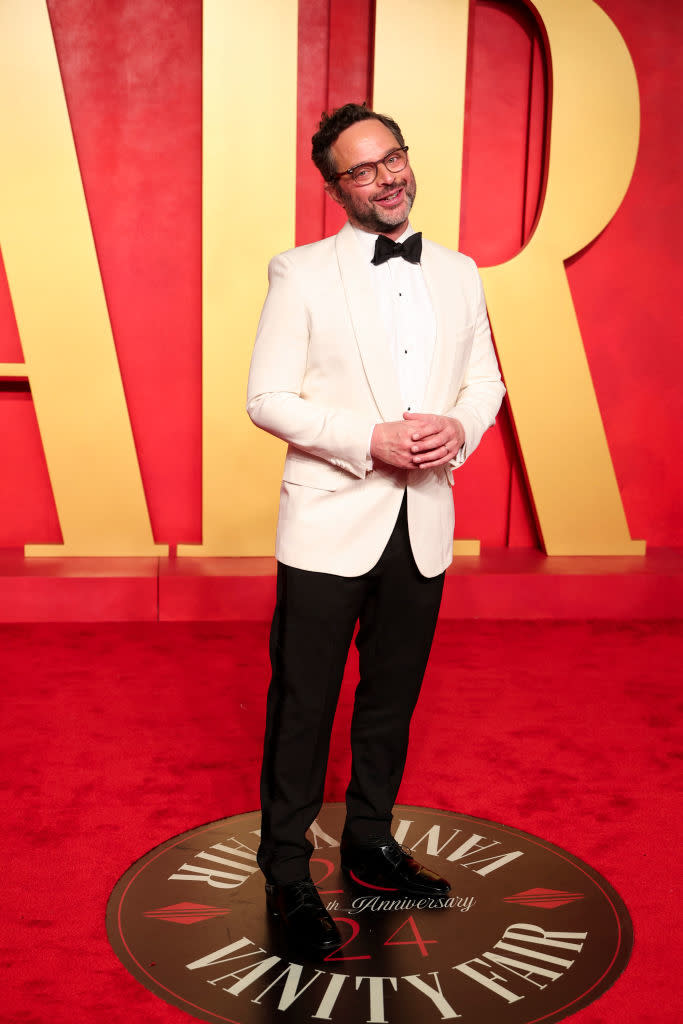 Man in a white jacket and black bow tie standing on the Vanity Fair red carpet