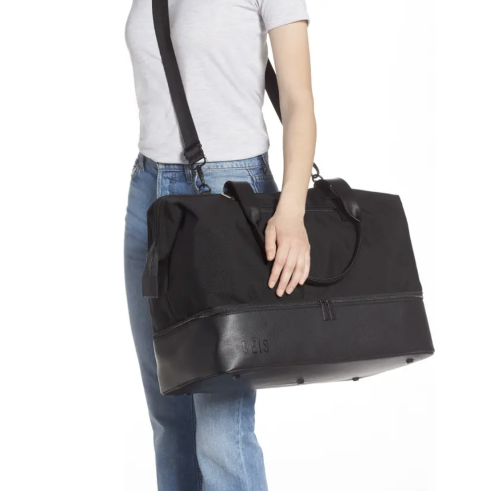 Model using the crossbody strap to hold a black zippered duffel bag with handles