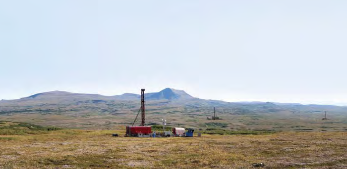 Drill rig in a tundra field with hills in the background.