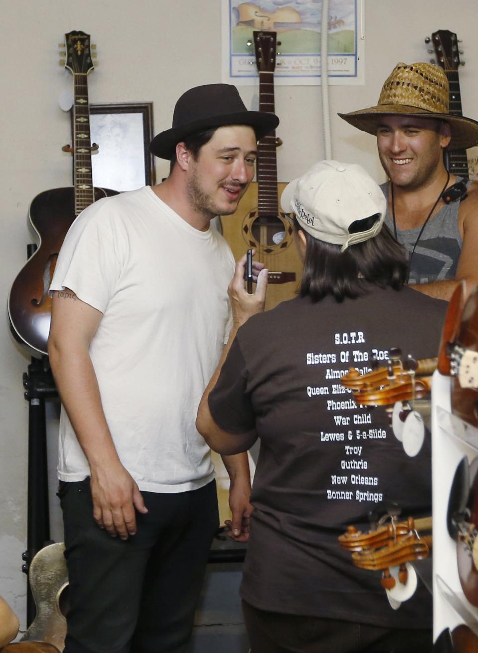 In this Sept. 5, 2013, photo Marcus Mumford, of the band Mumford & Sons, talks with Lucy Swanson, center, executive assistant for the Guthrie Chamber of Commerce, as he visits the Double Stop Fiddle Shop in Guthrie,, Okla. The population of the small Oklahoma town is expected to quadruple this weekend as people come to watch the British folk rock band on the second stop of the Mumford & Sons’ Gentlemen of the Road concert series in Guthrie. At right is Kevin Bilvin. (AP Photo/Sue Ogrocki)