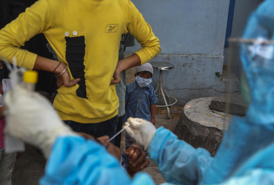 A child wearing a mask as a precaution against the coronavirus watches as a health worker takes a nasal swab sample of a woman to test for COVID-19 at a hospital in Hyderabad, India, Monday, April 19, 2021. (AP Photo/Mahesh Kumar A.)