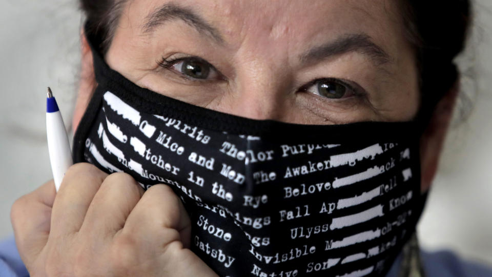 Poet Tammi Truax poses at her writing table, wearing a protective mask due to the COVID-19 virus outbreak, Wednesday, July 29, 2020, at her home in Eliot, Maine. Truax, the poet laureate for Portsmouth, N.H., pens a weekly pandemic poem that is included in the city's COVID-19 newsletter. (AP Photo/Charles Krupa)