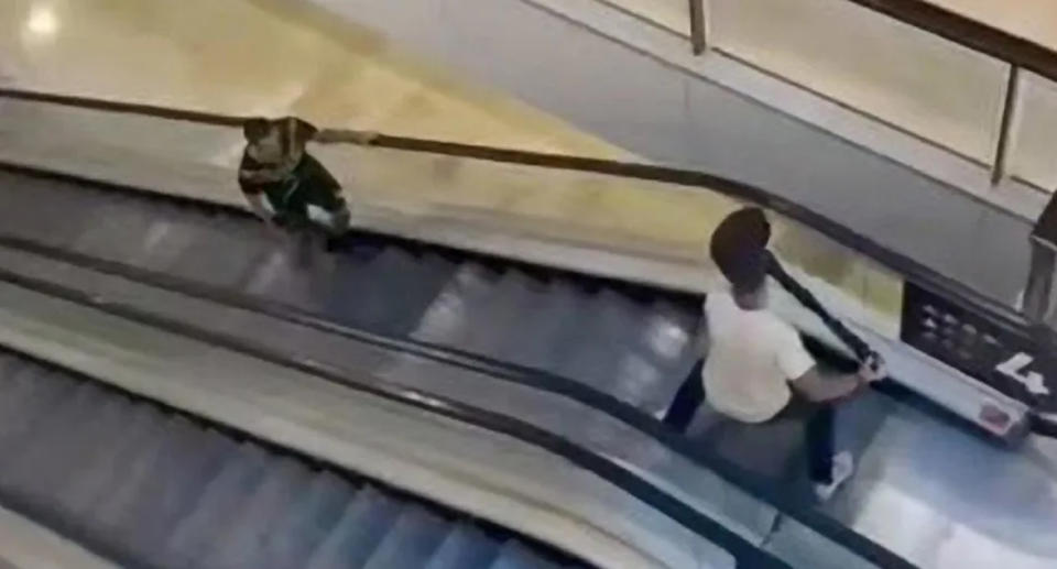 Damien Guerot in a white t-shirt standing at the top on an escalator holding a bollard fighting off Bondi killer Joel Cauchi holding a knife. 