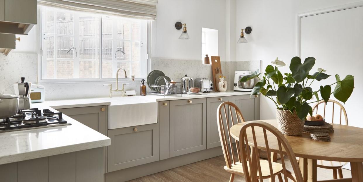 a grey toned kitchen with a wooden table and chairs softened with off white stripe blinds and brass handles