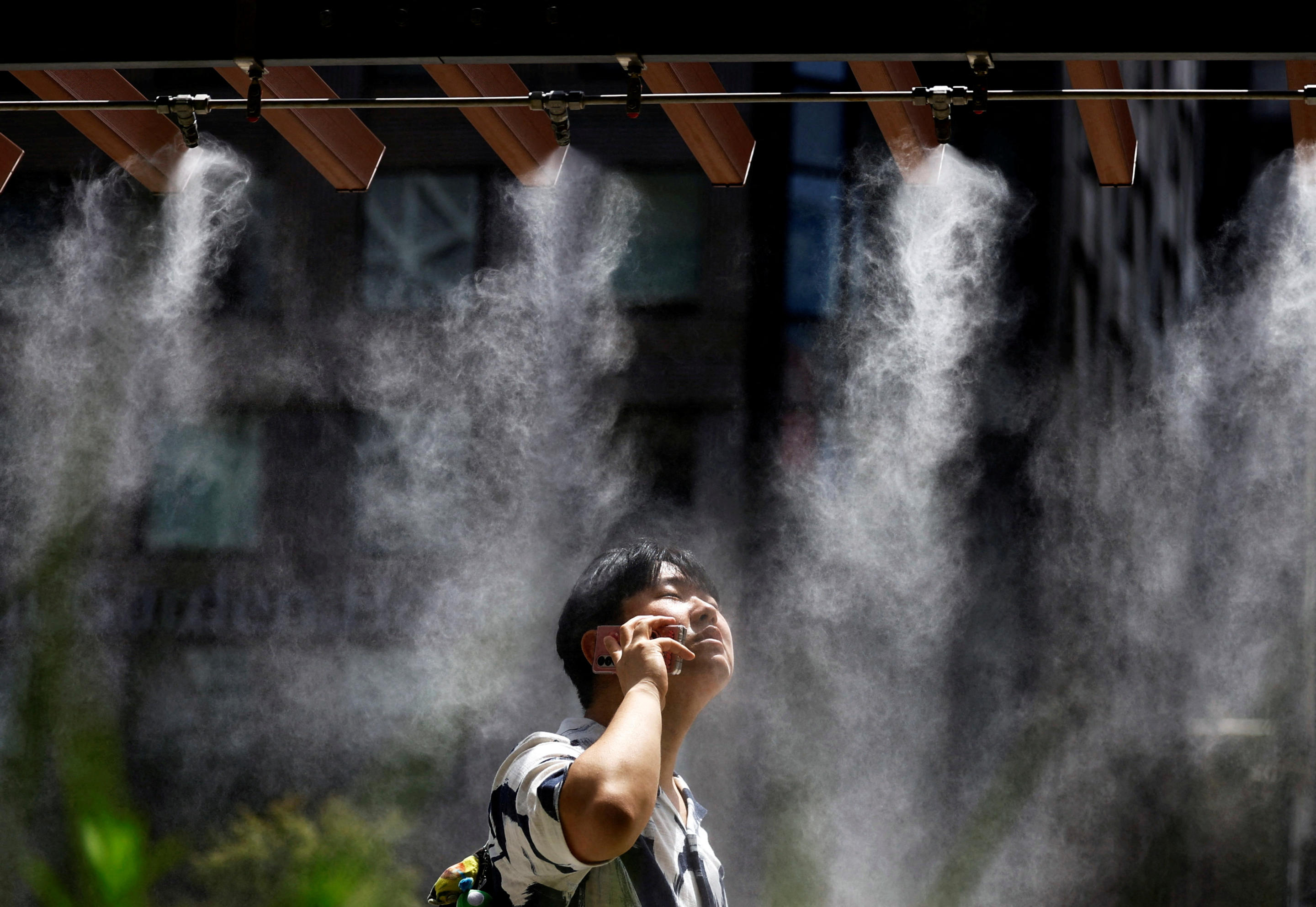 A man on his phone takes a break and stands under a cooling mist.