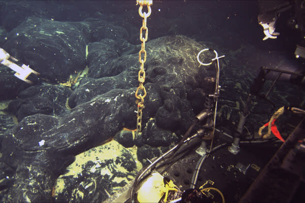 A chain still attached to an ocean-bottom hydrophone (OBH) comes directly out of the seafloor at Axial Seamount where a lava flow erupted in 2011 has buried the instrument to a depth of about 1.5 meters (5 feet). The front of the Jason remotely