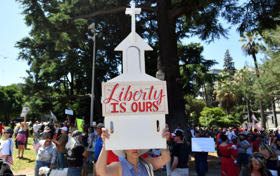 A woman help up a sign depicting a church as hundreds of people gathered earlier this month to protest the stay-at-home orders outside the state Capitol building in Sacramento.  (Photo: JOSH EDELSON via Getty Images)