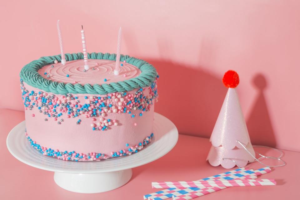 cake stand with strawberry birthday cake, drinking straws and party hats