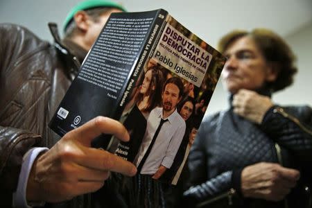 A man talks about a book he is holding, written by Pablo Iglesias, Secretary General of the party "Podemos" (We Can), to a woman at the end of their local assembly in Madrid's Salamanca district December 18, 2014. REUTERS/Susana Vera