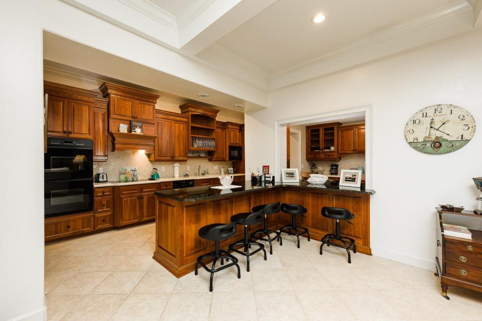 The open and spacious kitchen features custom wood cabinets, granite and Corian countertops, Dacor double ovens and five-burner cooktop, a new large Café fridge, a breakfast bar, a separate coffee bar area and two pantries.