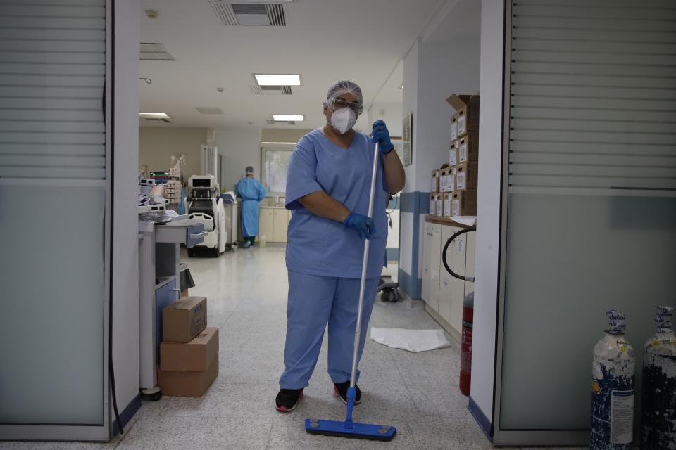 Cleaning worker Anthoula Dimitra Pagouni, 30, poses in an ICU entrance of the Sotiria Thoracic Diseases Hospital in Athens, Monday, Jan. 18, 2021. The cleaners of coronavirus intensive care units run a daily gauntlet of infection risks to ensure that ICUs run smoothly, and they are critical to preventing the spread of disease in hospitals. But their status as unskilled laborers in a behind-the-scenes role has left them out of the public eye. (AP Photo/Thanassis Stavrakis)