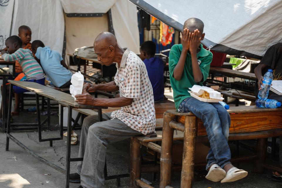 A man eats a meal as a child covers his face after receiving containers of free food at a shelter for families displaced by gang violence, in Port-au-Prince, Haiti, Thursday, March 14, 2024. (AP Photo/Odelyn Joseph)