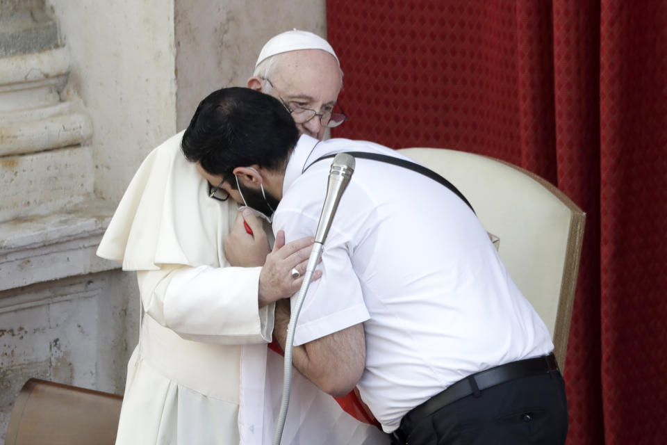 Pope Francis is hugged by Lebanese priest Georges Breidi, right, as they hold a Lebanese flag in remembrance of last month's explosion in Beirut, during the pontiff's general audience, the first with faithful since February when the coronavirus outbreak broke out, at the San Damaso courtyard, at the Vatican, Wednesday, Sept. 2, 2020. (AP Photo/Andrew Medichini)