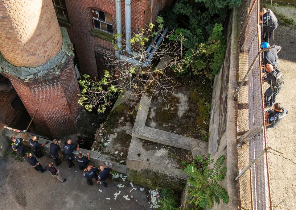 Officers above watch as others make their way to a man hiding behind a smokestack near the Denholm Building.