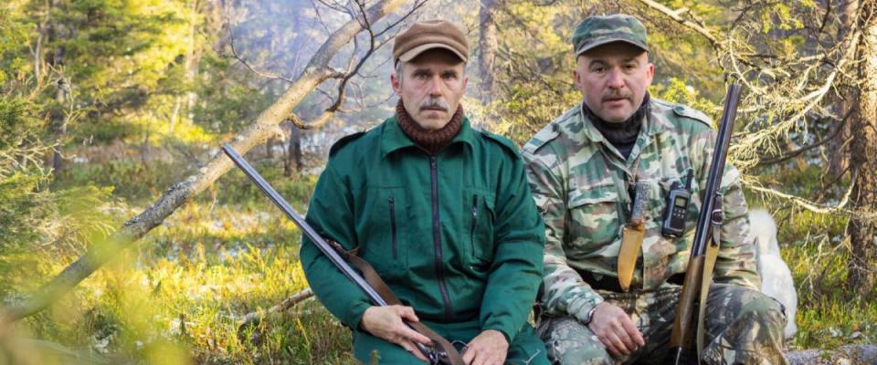 Two older hunters rest, sitting on a log