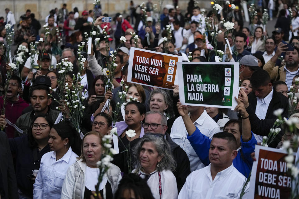 People hold flowers and signs during an event to remember former guerrillas and social leaders who have been killed since the 2016 signing of a peace agreement between rebels of the Revolutionary Armed Forces of Colombia, FARC, and the government, in Bogota, Colombia, Tuesday, Feb. 20, 2024. (AP Photo/Fernando Vergara)