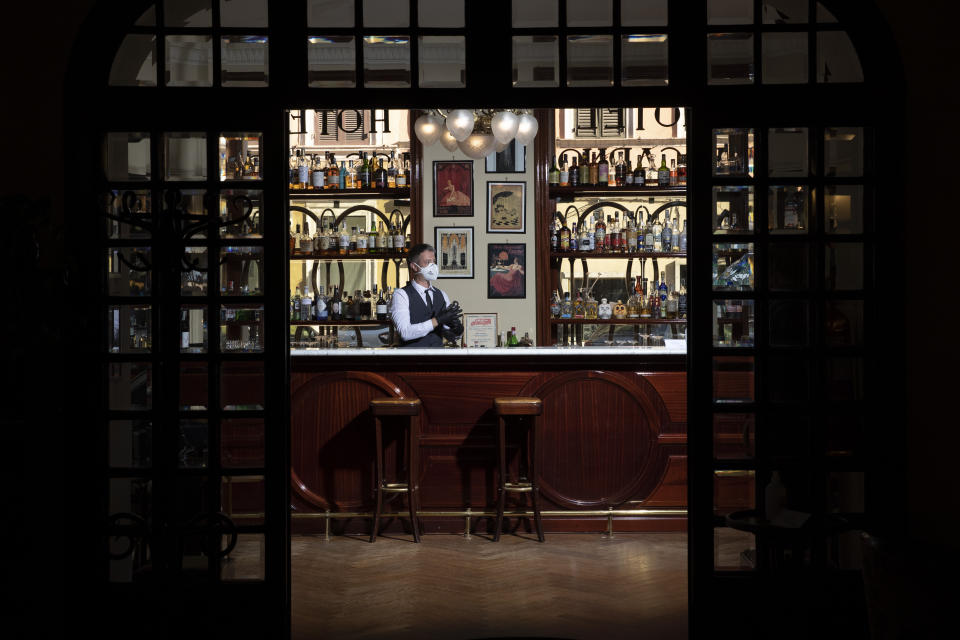 In this Monday, May 11, 2020 photo, barman Nicholas Pinna wears a protective face mask as he stands behind the cocktail bar of the art-deco style Locarno Hotel, in Rome, Monday, May 11, 2020. Pinna is looking forward to a return to normality, he says he has "lots of hope to restart soon, to see again all our clients which we were used to see here, and to return to working with maximum serenity” as the hotel prepares to welcome back its clients, hopefully soon. (AP Photo/Alessandra Tarantino)