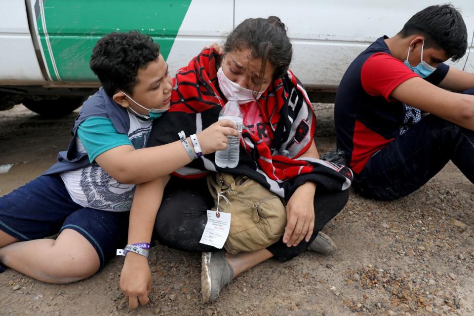 A boy offers his mother a water bottle as they sit beside another boy.