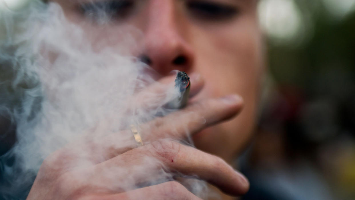  Closeup of a man smoking a joint outdoors, as he blows out a large plume of smoke. 