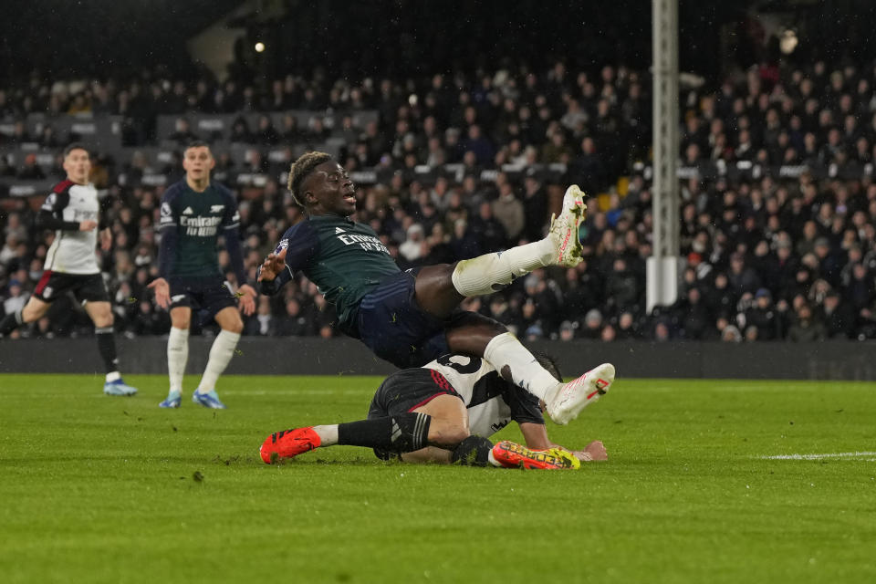 Arsenal's Bukayo Saka loses his balance after he was challenged by Fulham's Joao Palhinha, on ground, during the English Premier League soccer match between Arsenal and Fulham at Craven Cottage stadium in London, Sunday, Dec. 31, 2023. (AP Photo/Alastair Grant)