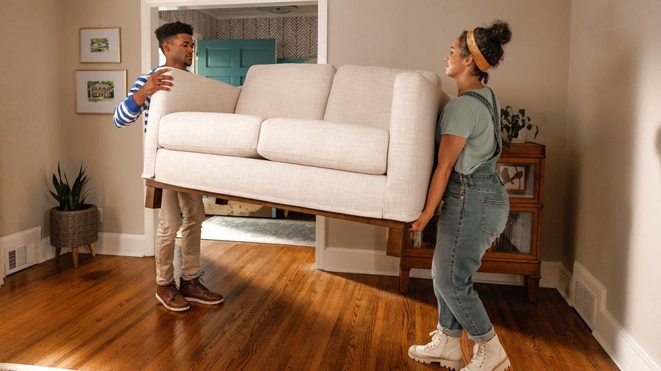 A young couple lifting a couch and moving into a new place.