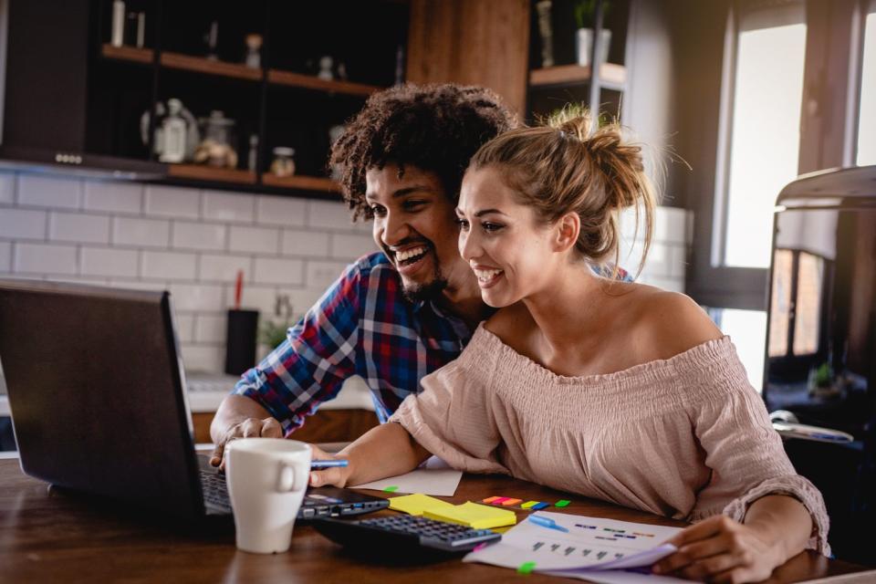 Two investors smiling and looking at something on a laptop in the living room.