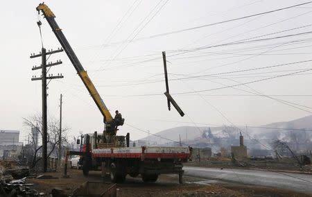 A worker operates a mobile crane while lifting a burnt electric line mast in the settlement of Shyra, damaged by recent wildfires, in Khakassia region, April 13, 2015. REUTERS/Ilya Naymushin