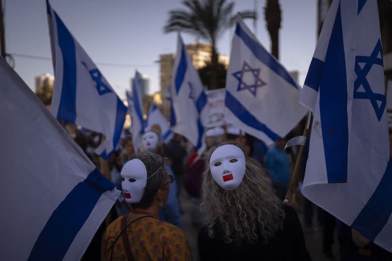 Manifestantes usan máscaras y ondean banderas israelíes durante una protesta contra los planes del gobierno del primer ministro Benjamin Netanyahu para reformar el sistema judicial en Tel Aviv, Israel, el martes 28 de marzo de 2023. (AP/Oded Balilty)