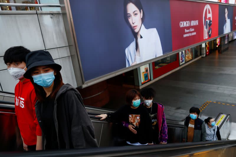 People wearing protective masks walk in a shopping district in Beijing