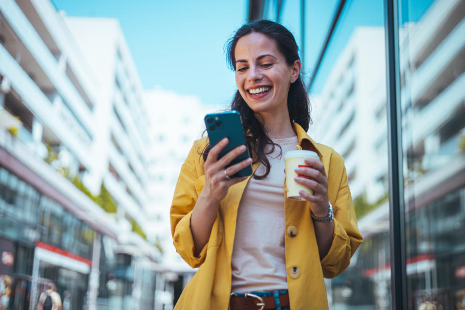 Woman texting and drinking coffee outdoors. Artificial intelligence and communication network concept.Beautiful young woman using a smartphone.