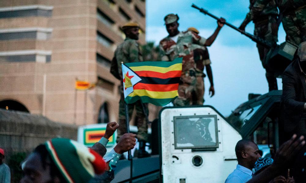 A man holds up the national flag of Zimbabwe as soldiers are cheered in the streets in Harare