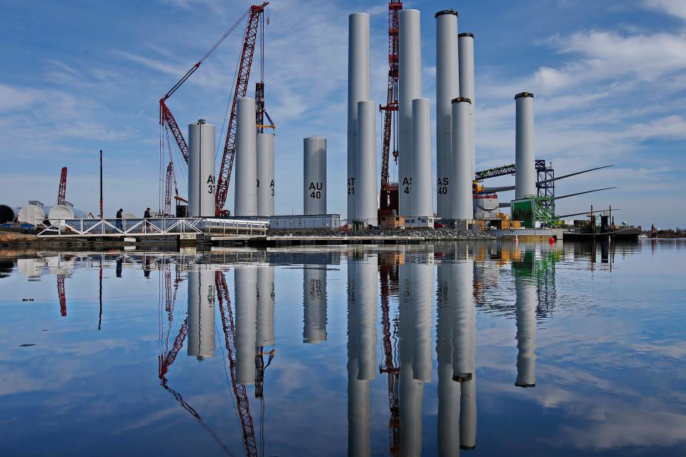 Two men walk across the bridge to the dock in front of the wind turbine towers for the Vineyard Wind offshore wind farm being assembled at the New Bedford Marine Commerce Terminal.