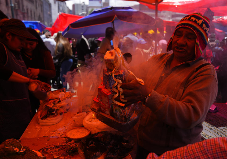 Un brujo indígena aymara bendice miniaturas de comida para un cliente durante la feria anual de Alasita en el centro de La Paz, Bolivia, el miércoles 24 de enero de 2024. En el día de inauguración de la feria se ofrecen réplicas en miniatura de las cosas que las personas anhelan o desean, como casas, vehículos o salud, para que se conviertan en realidad. Alasita es una palabra aymara que significa "cómprame". (AP Foto/Juan Karita)