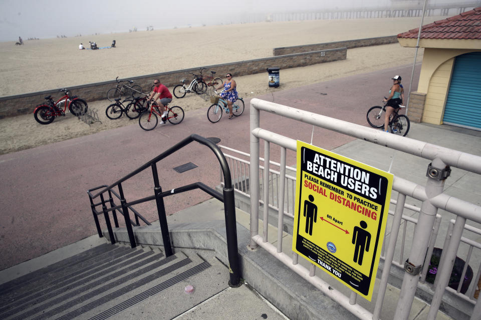 FILE - In this April 26, 2020, file photo, a sign encourages people to practice social distance in Huntington Beach, Calif. As the weather warms, some already have begun venturing outside in larger numbers, despite guidance to stay home. Government officials say they aim to manage public health risks in a way that allows for a gradual return to normal, but with the course of the outbreak still unknown, nobody is sure what summer will bring. (AP Photo/Marcio Jose Sanchez, File)