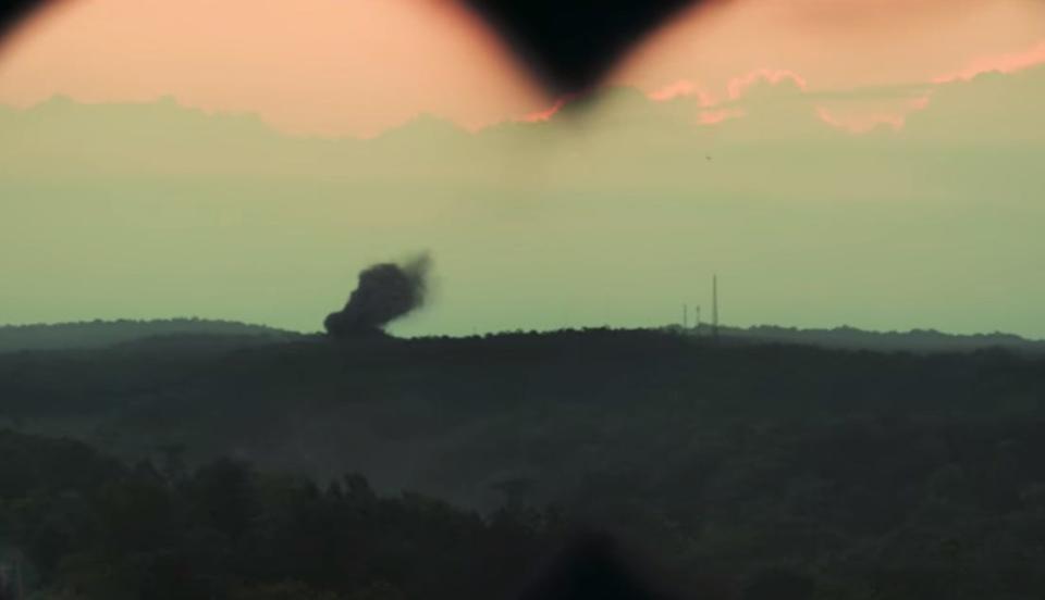 A still from the film version of White Noise. Here, Adam Driver’s character uses binoculars to inspect the rising smoke from the crash.