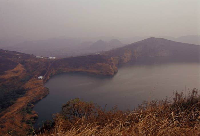 A hazy landscape photo shows the shores of a large, calm lake surrounded by hills and sparse vegetation